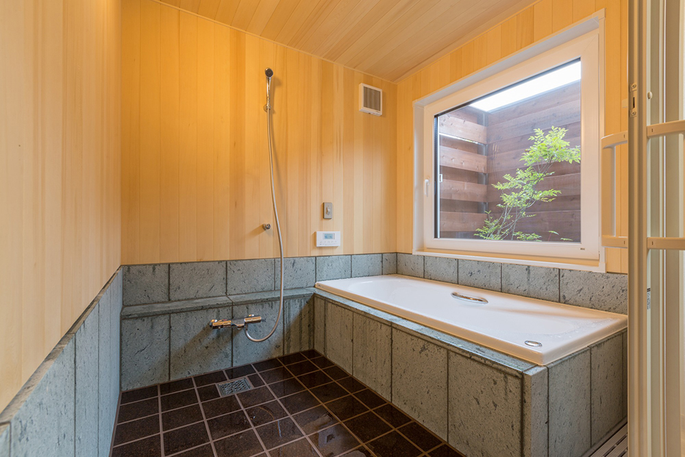ヒバの薫る浴室。腰壁は濡れると緑色に美しく変わる十和田石で、床は暖かく柔らかいコルクタイル。